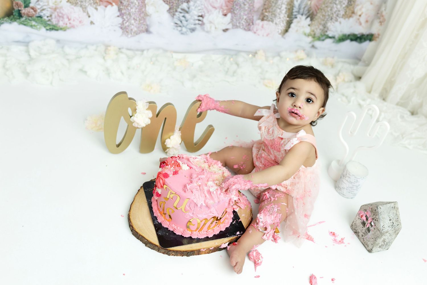 Festive cake smash photography setup with pink tutu and gold decorative elements.