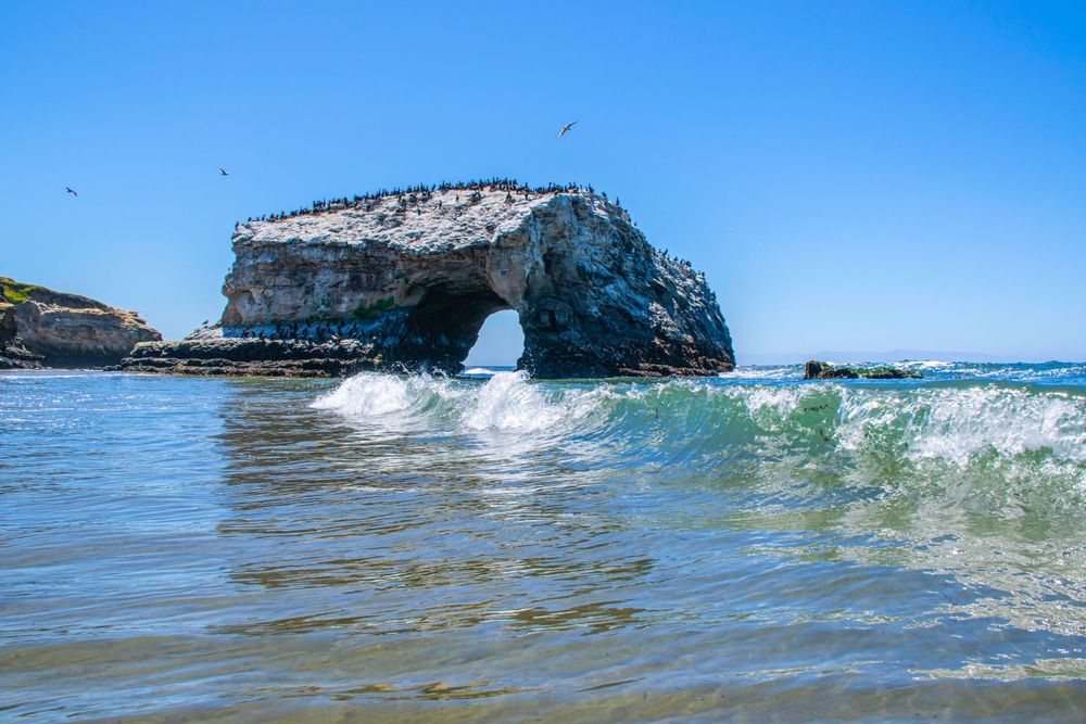 Ocean waves crash near Natural Bridge Rock formation at Santa Cruz beach.