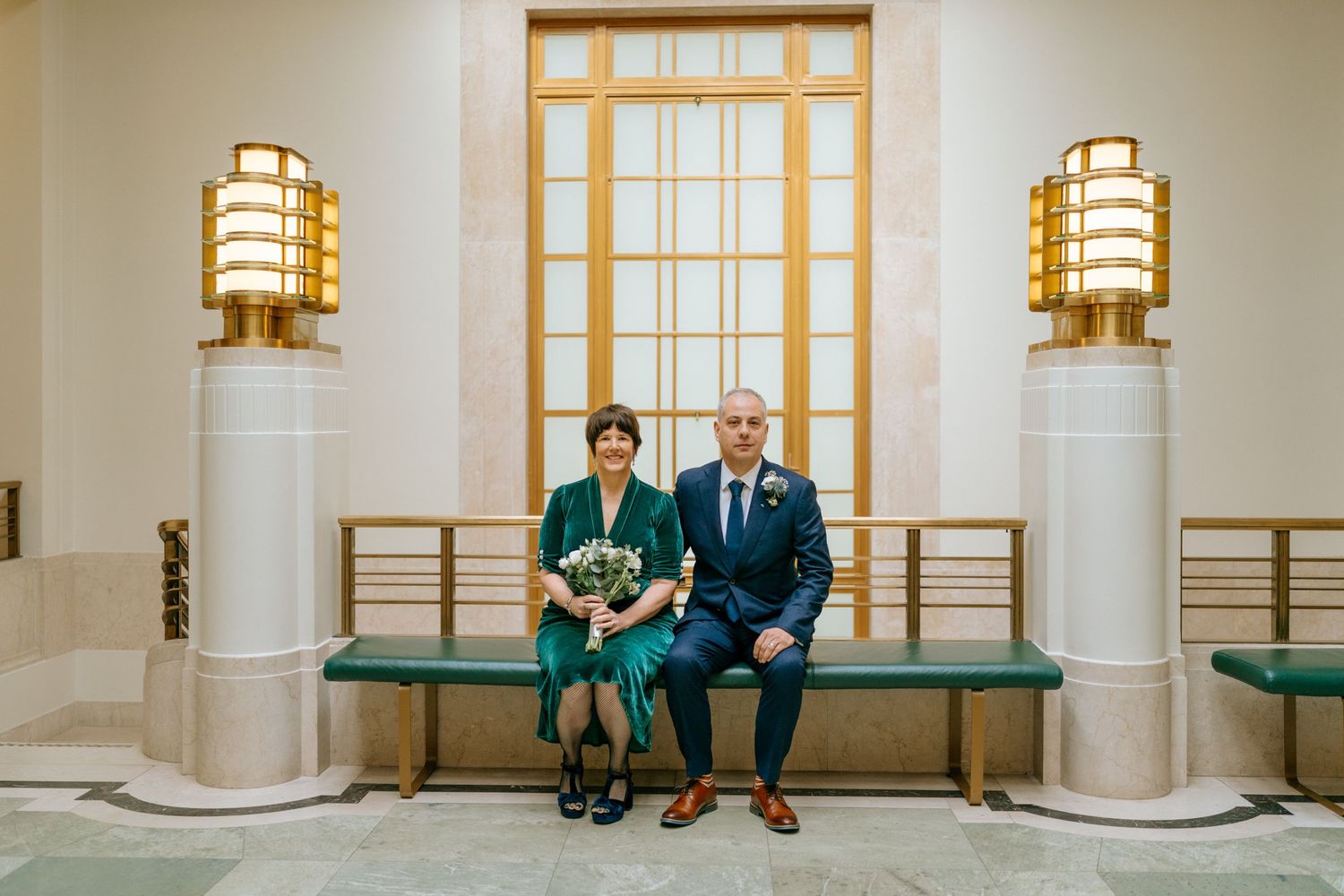 Couple sitting on bench in elegant venue with art deco lighting fixtures.