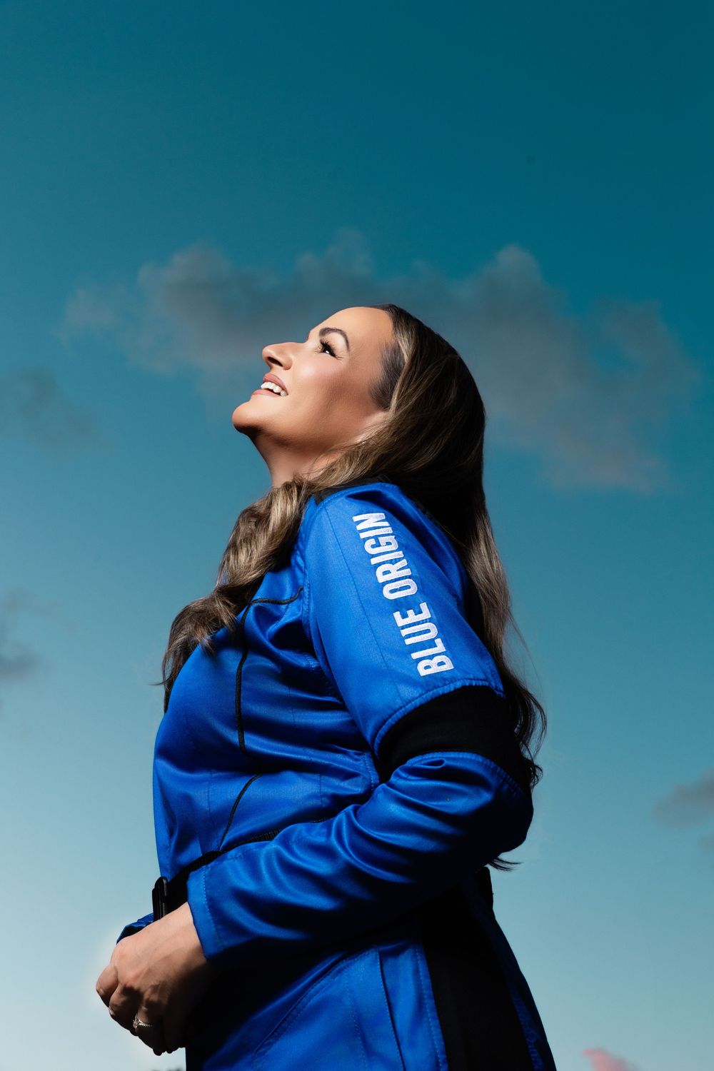 Woman in Blue Origin spacesuit gazing upward against a blue sky, conveying wonder and aspiration.