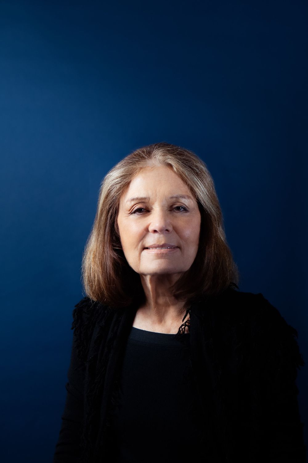 Portrait of a woman with shoulder-length brown hair wearing black against a dark blue background.