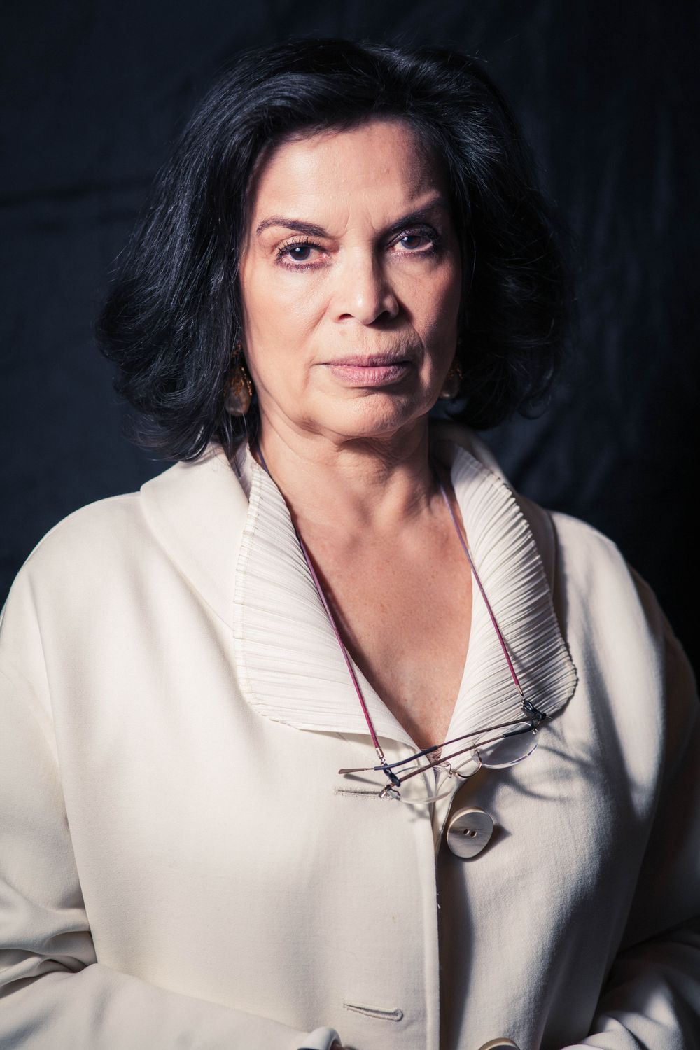 Portrait of person in cream-colored blazer against dark background.
