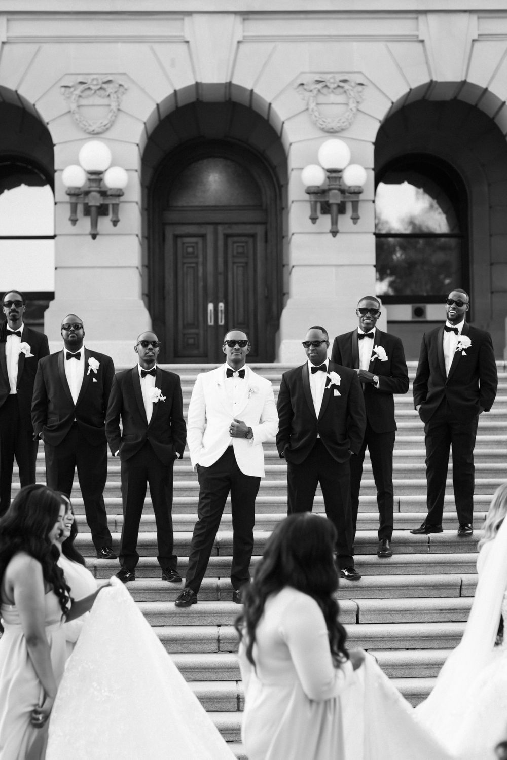 Wedding party formal portrait with groomsmen in black tuxedos on stone steps.