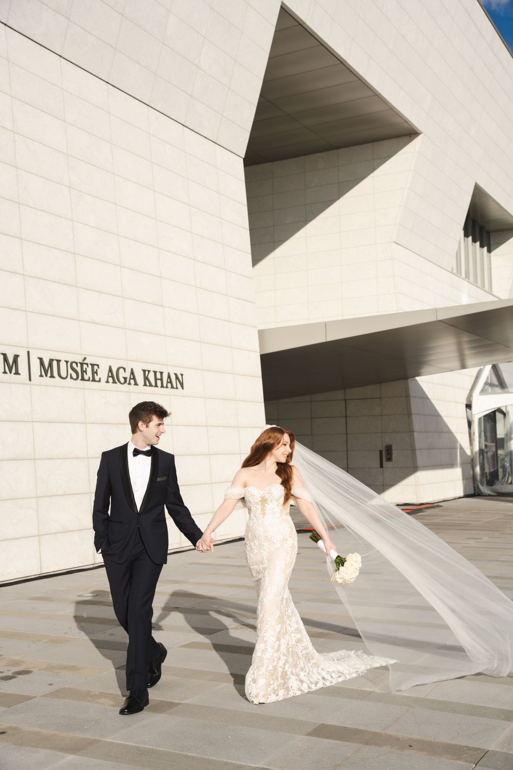 Wedding couple walking hand in hand outside the modern architecture of Musée Aga Khan.