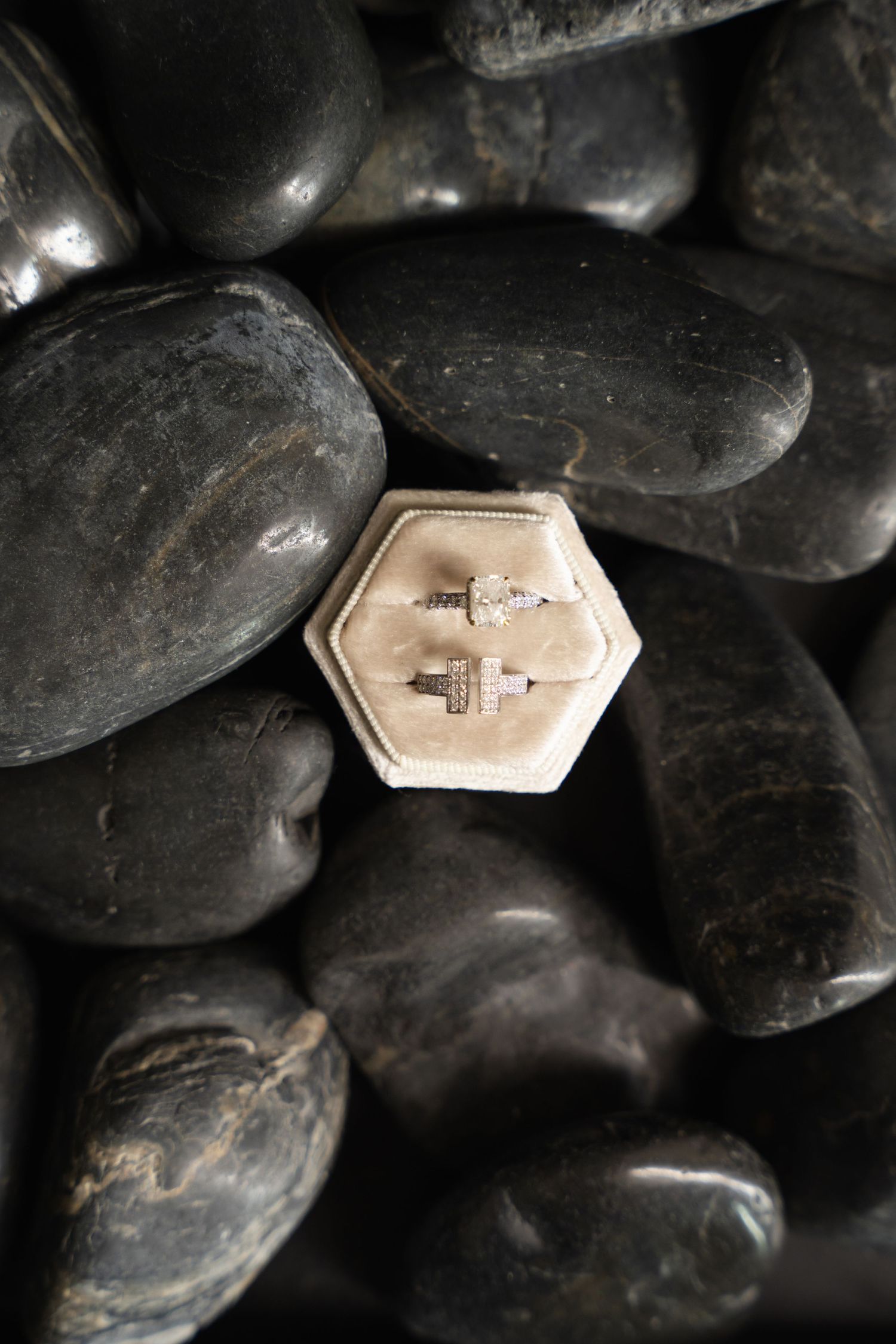 Wedding rings displayed in hexagonal box on black stones for dramatic effect.