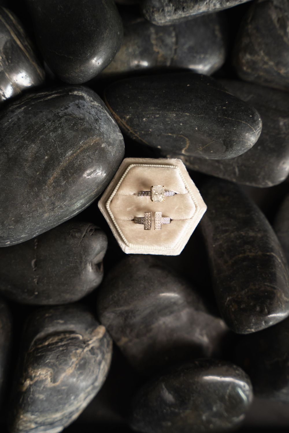 Wedding rings displayed in hexagonal box on black stones for dramatic effect.