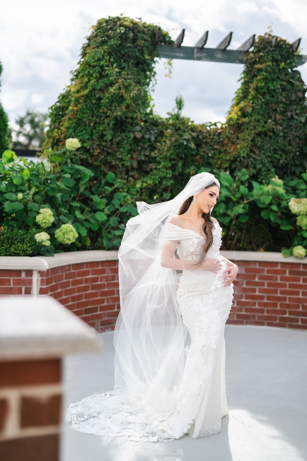 Bride twirls her dress on an elegant terrace surrounded by greenery and brick walls.