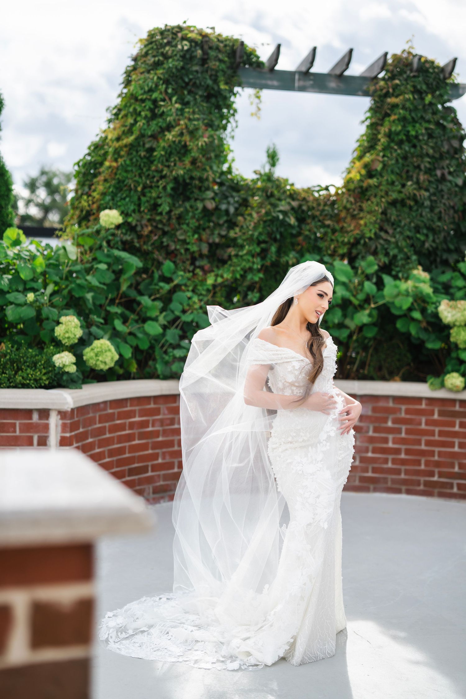 Bride twirls her dress on an elegant terrace surrounded by greenery and brick walls.
