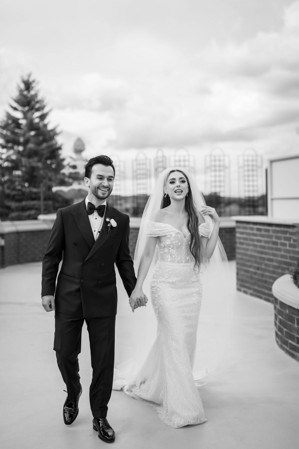 Black and white wedding photography of couple walking together on rooftop terrace.