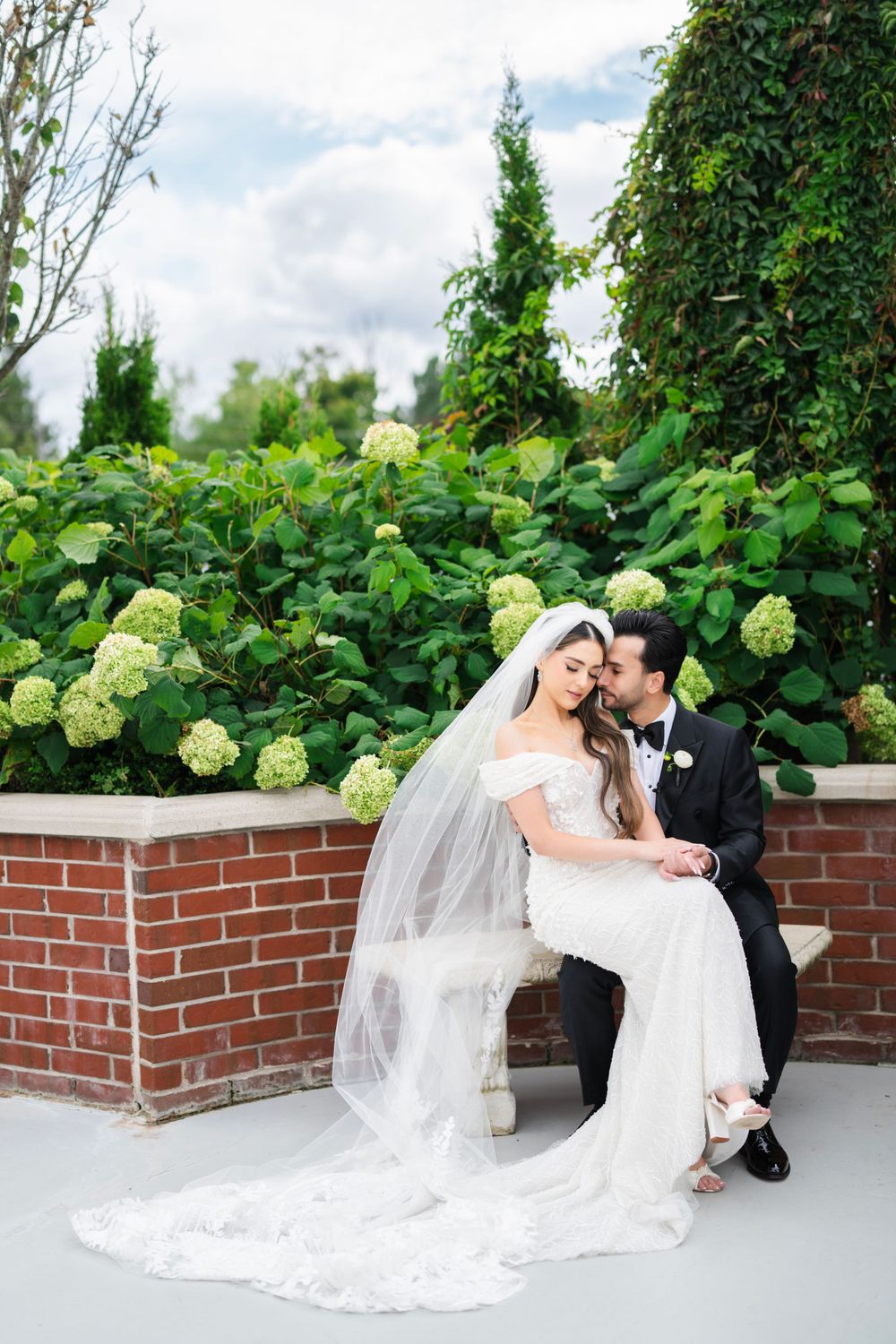Romantic wedding portraits against lush green hydrangea backdrop on brick terrace.
