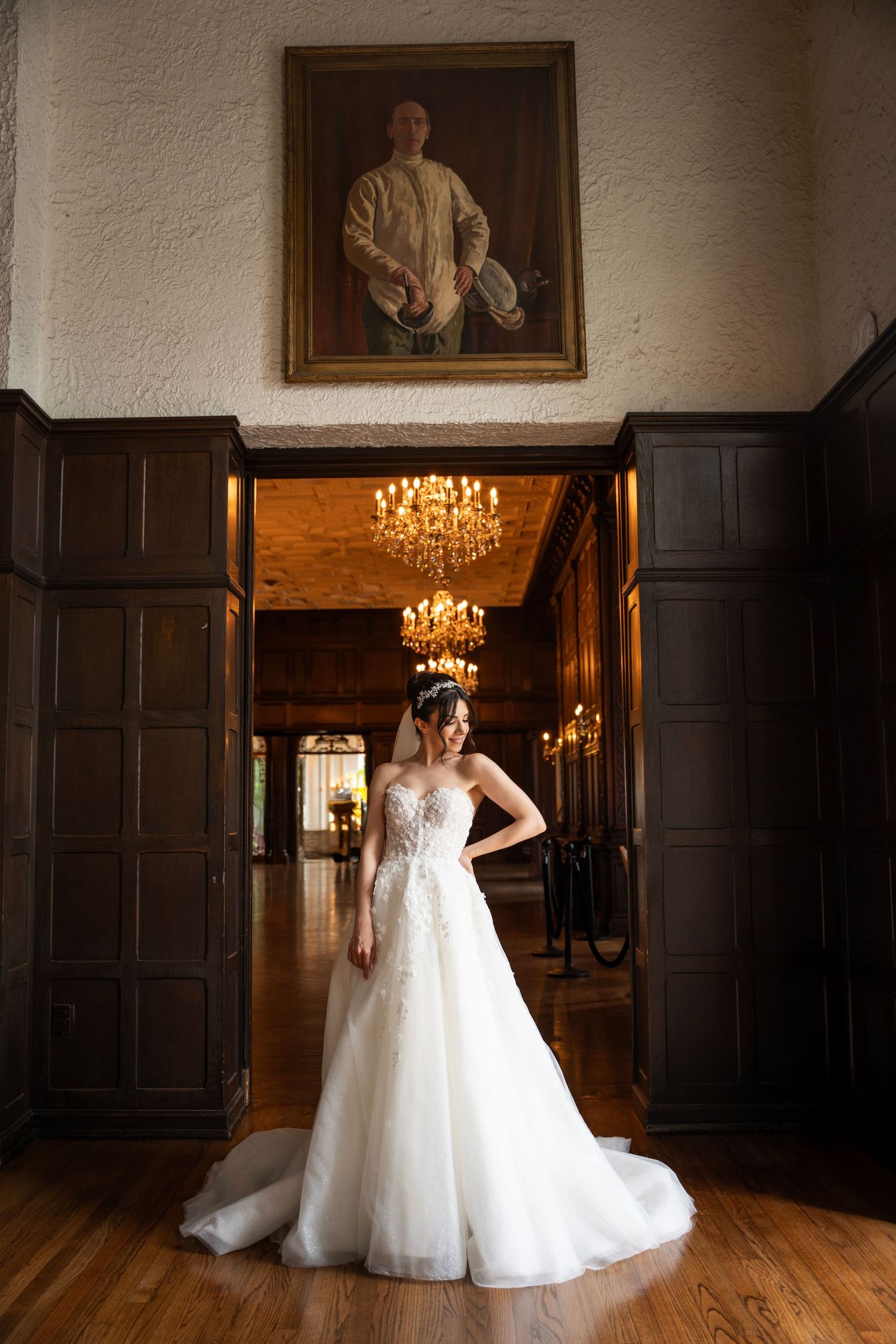 A ballgown wedding dress twirls in a historic wood-paneled room with chandelier lighting.