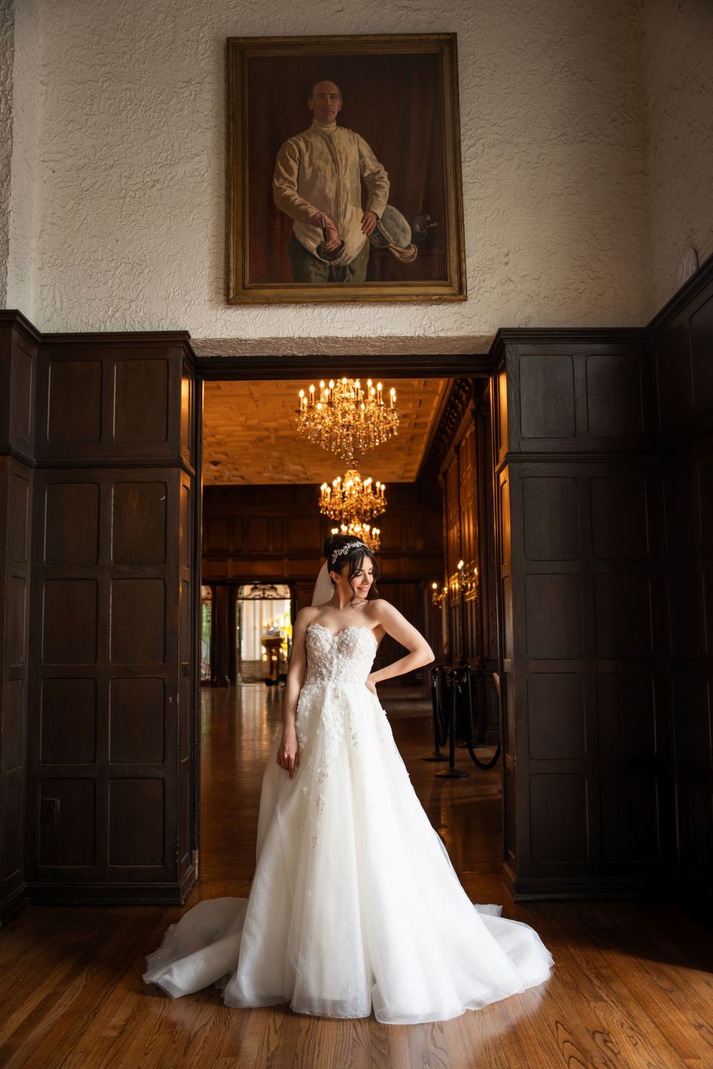 A ballgown wedding dress twirls in a historic wood-paneled room with chandelier lighting.