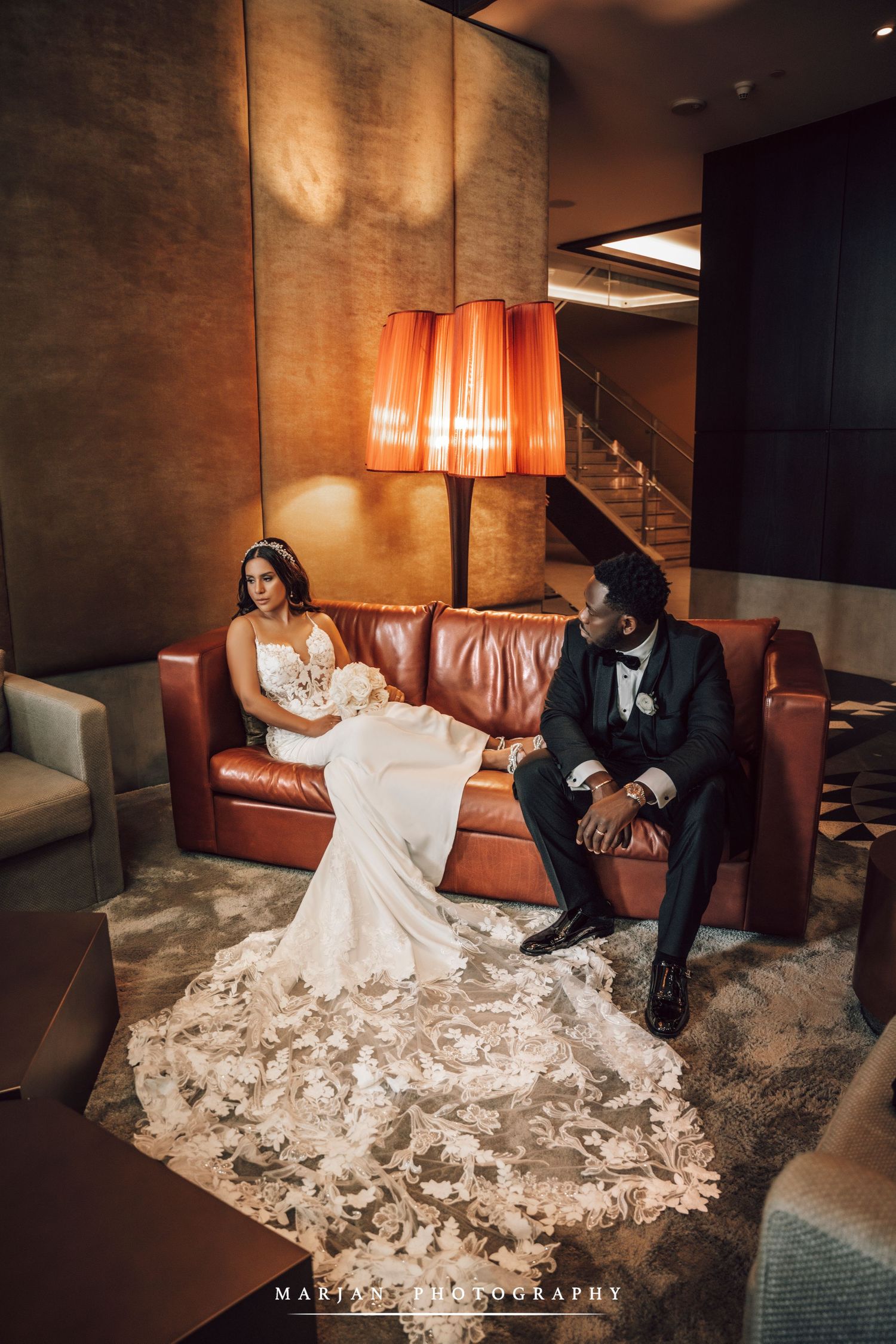 Newlyweds relaxing on leather couch in moody hotel lounge setting.