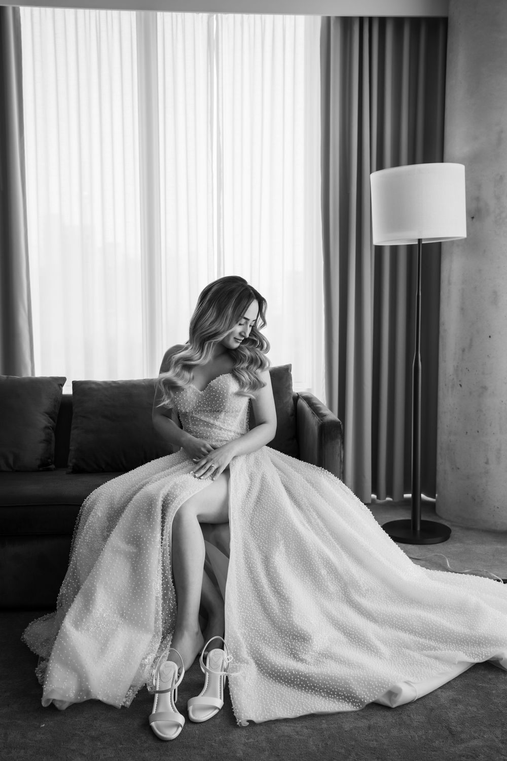 Black and white portrait of bride in elegant ballgown sitting by window.