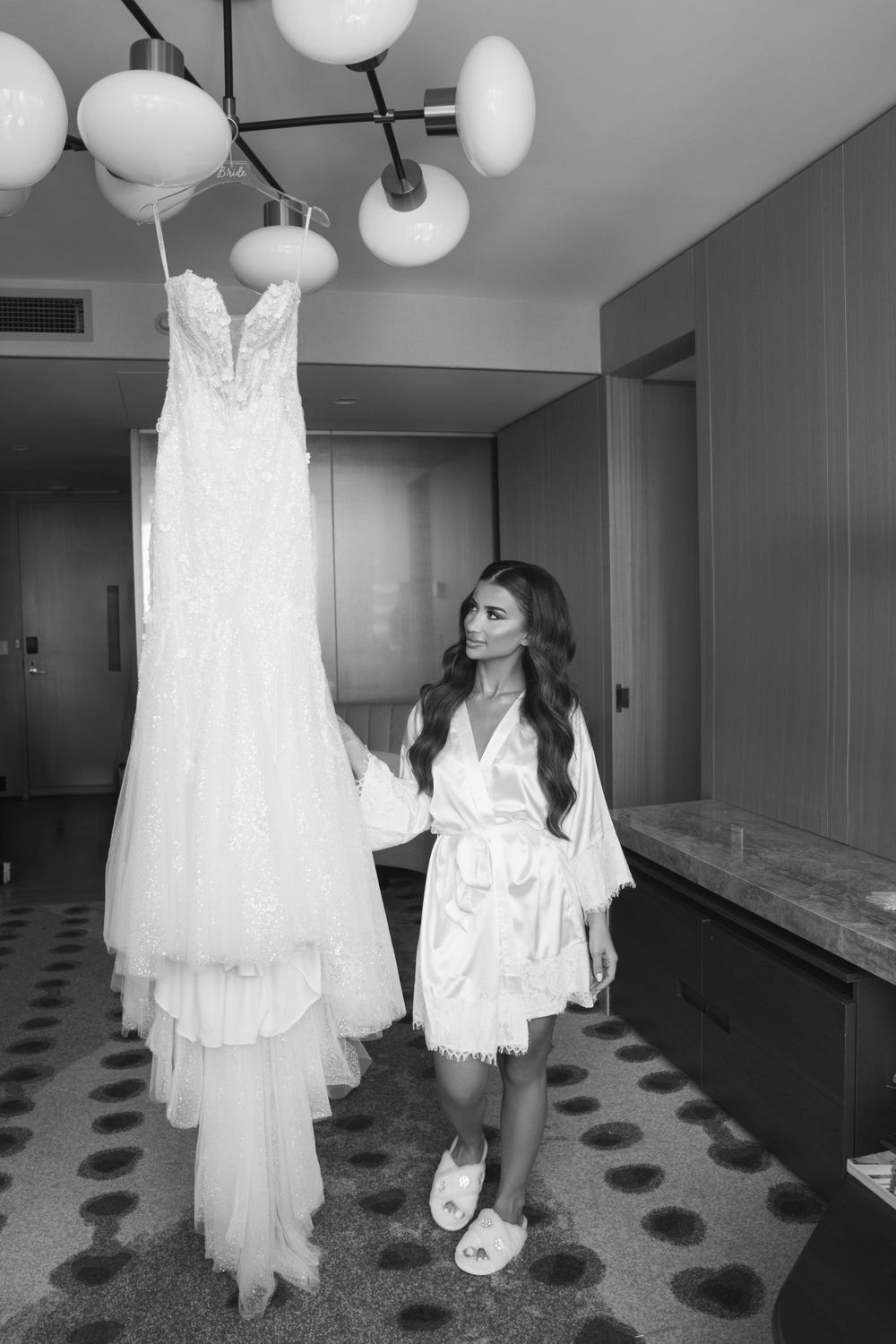 Black and white photo of wedding dress preparation in a hotel hallway with paper lanterns.