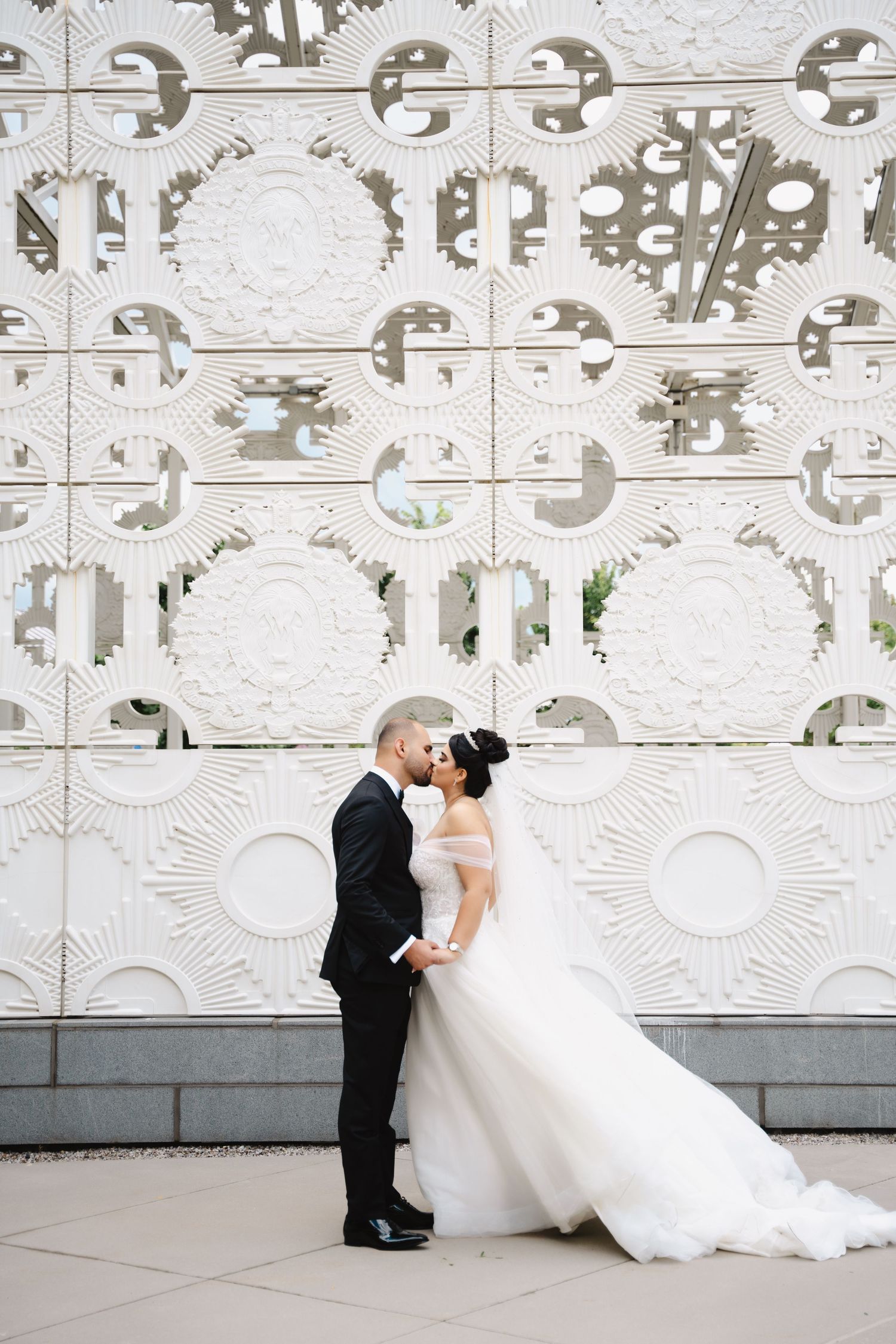 Wedding couple shares intimate moment against ornate white architectural wall.