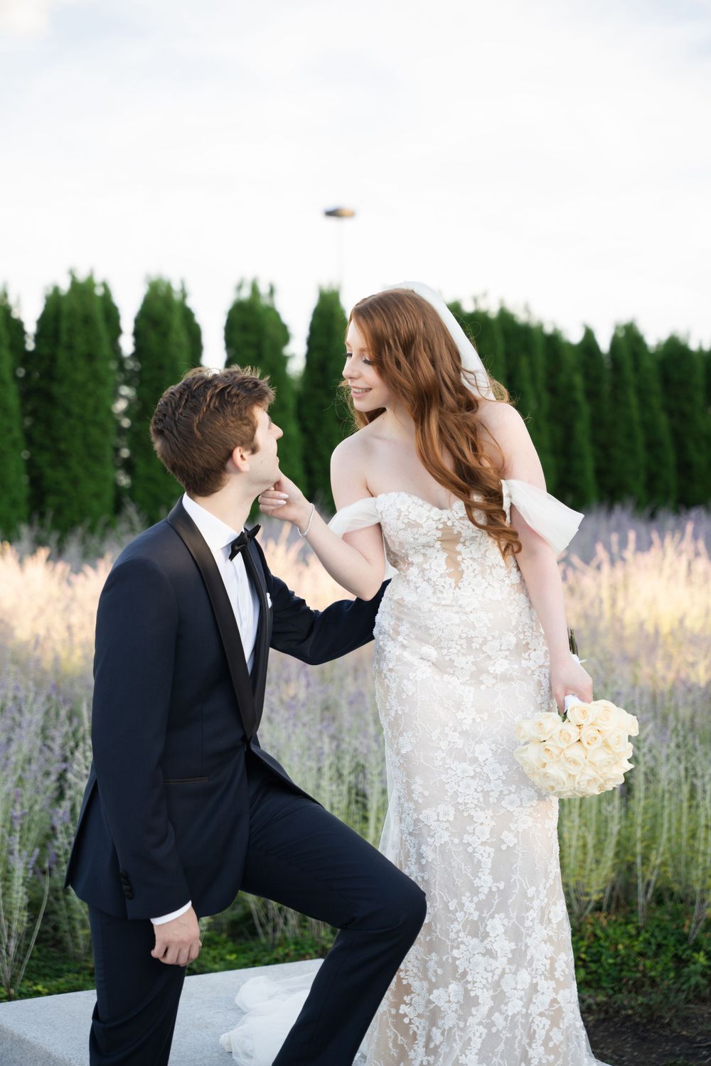 Playful wedding couple poses in field of lavender with groom on one knee.