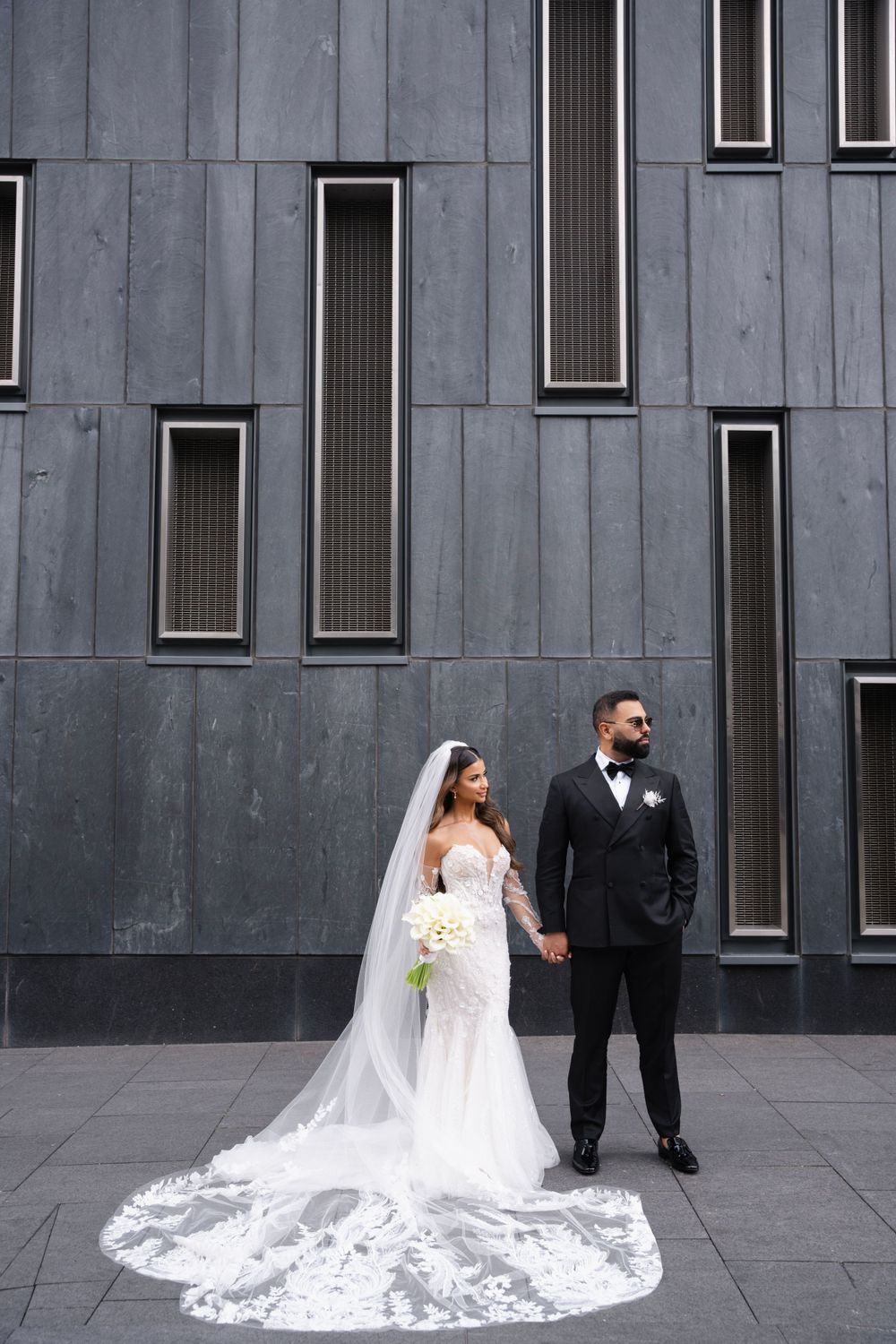 Dramatic wedding photos against modern grey architectural backdrop with flowing veil.