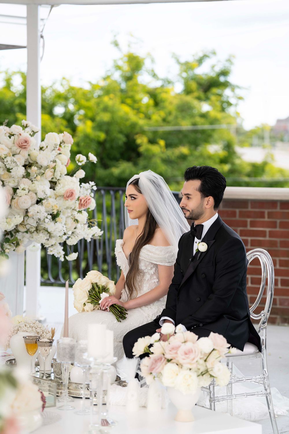 Newlyweds seated at an elegantly decorated wedding reception table with white floral centerpieces.