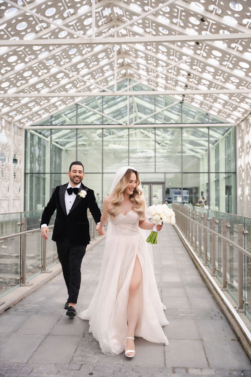 Happy couple walking through modern glass corridor with geometric lattice ceiling.