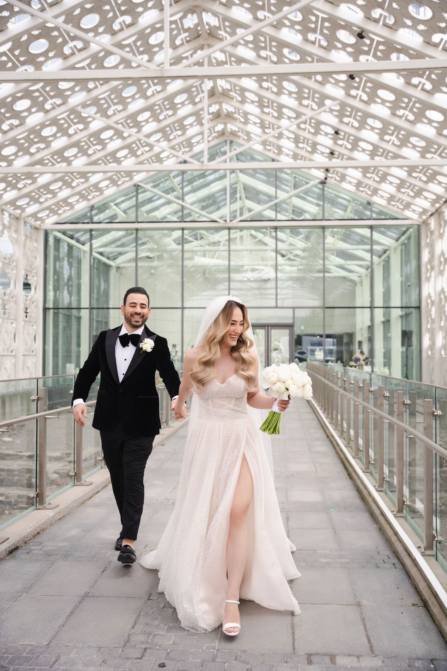 Happy couple walking through modern glass corridor with geometric lattice ceiling.