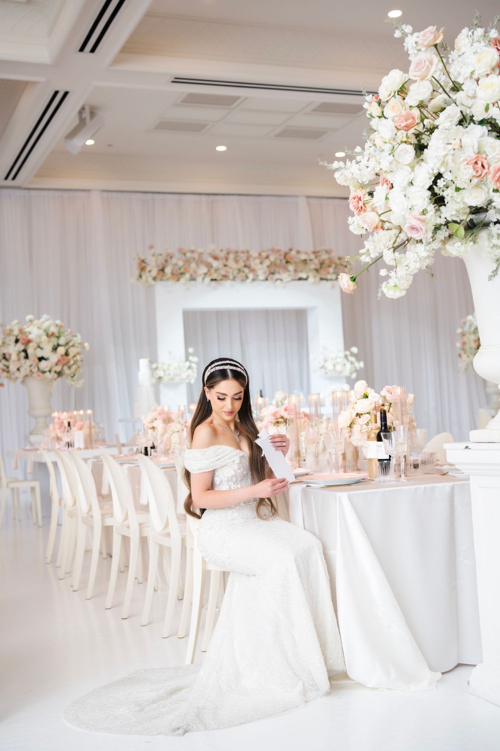 Bride poses in elegant white dress at beautifully decorated reception with floral arrangements.