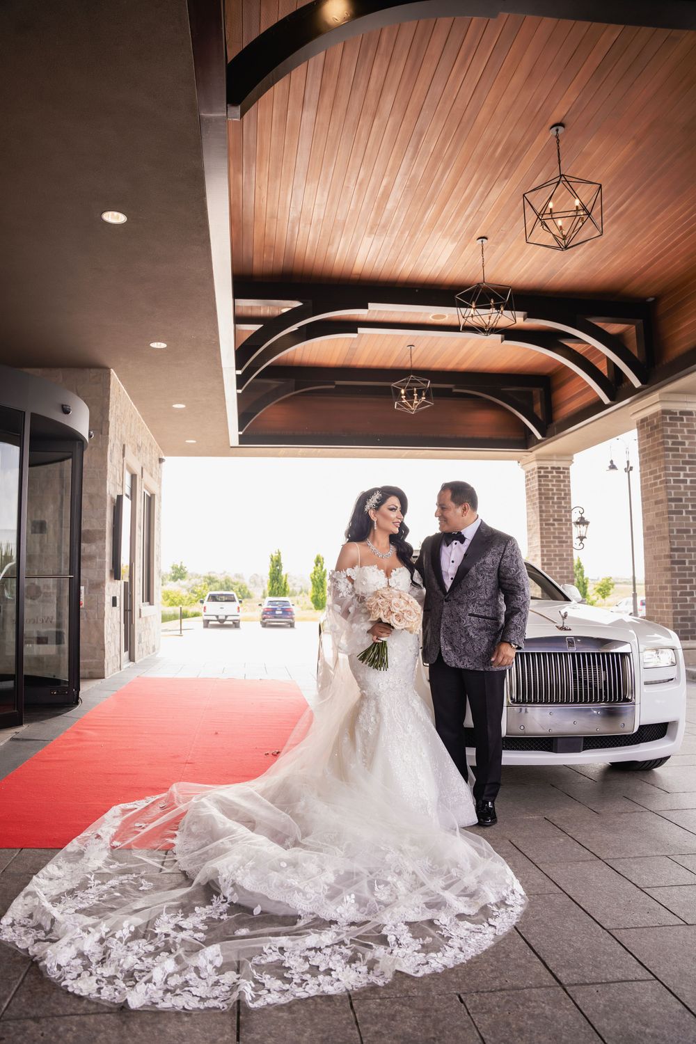 Dramatic wedding dress train spread across red carpet under wooden beamed portico.