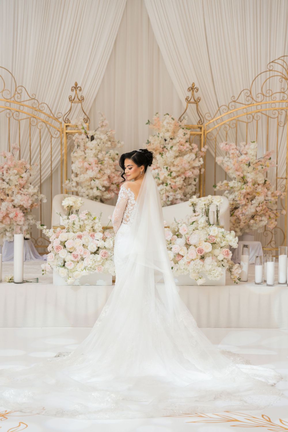 Elegant wedding reception hall decorated with soft pink and white floral arrangements and gold accents.