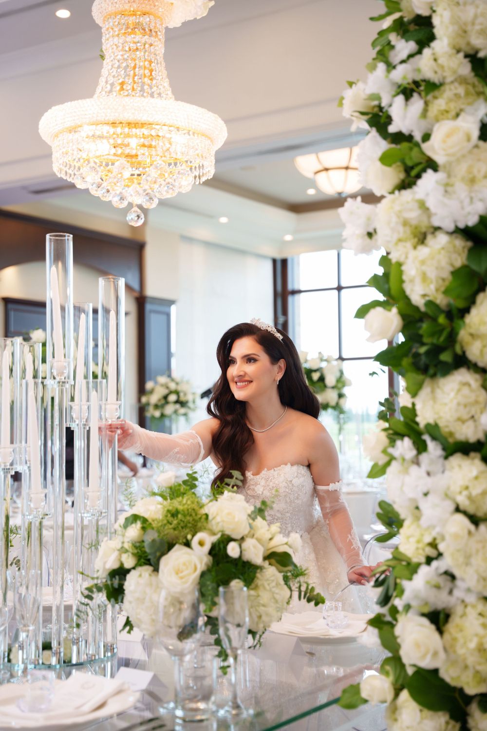 Elegant reception table with crystal chandelier, glass decor and white floral arrangements.