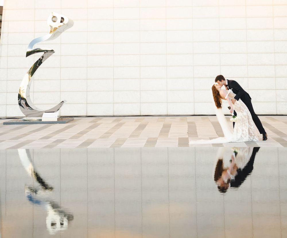 Wedding couple reflected in mirrored surface against white architectural wall.