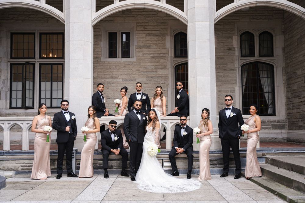 Wedding party in formal attire poses on stone steps of historic building.