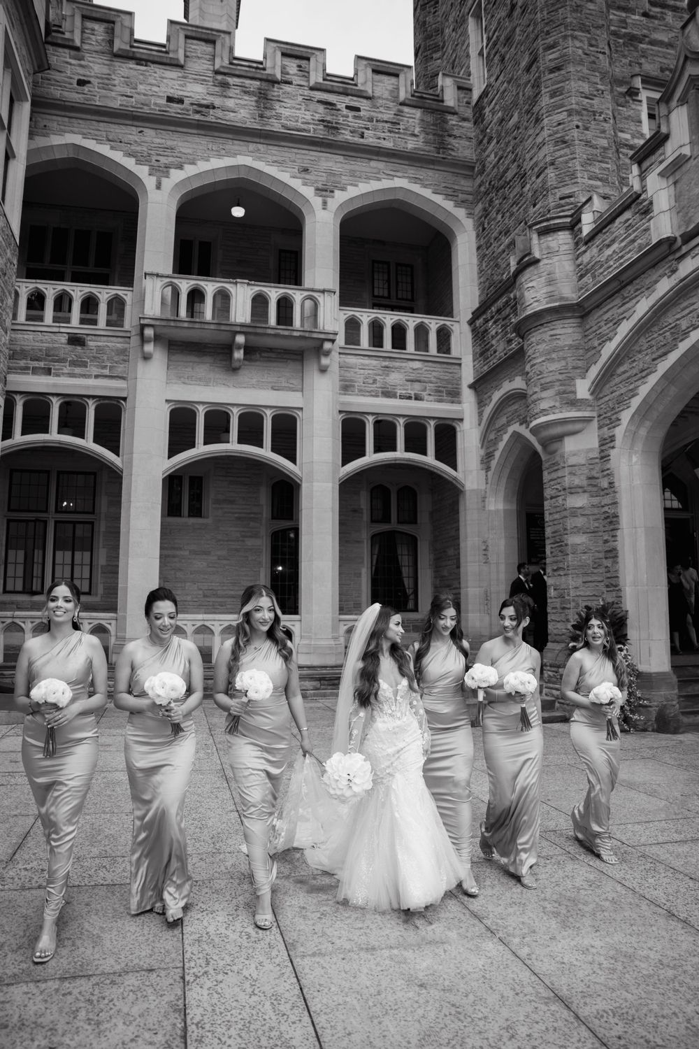 Wedding party runs playfully through a stone courtyard with gothic architecture.