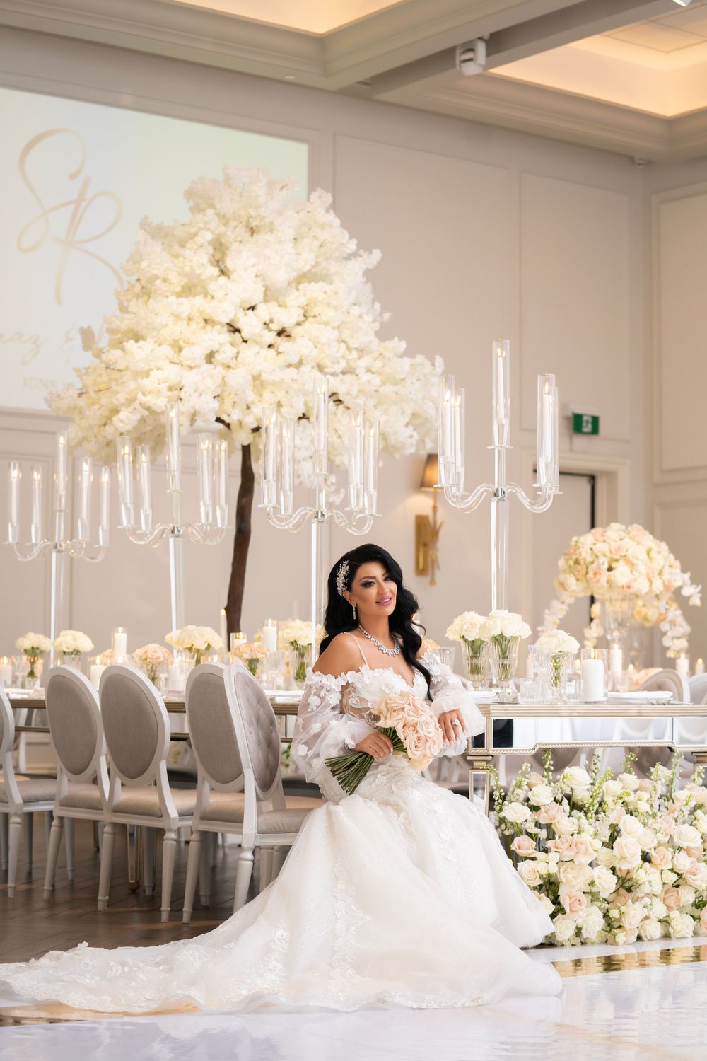 Luxurious white wedding reception tables with tall floral centerpieces and crystal candelabras.