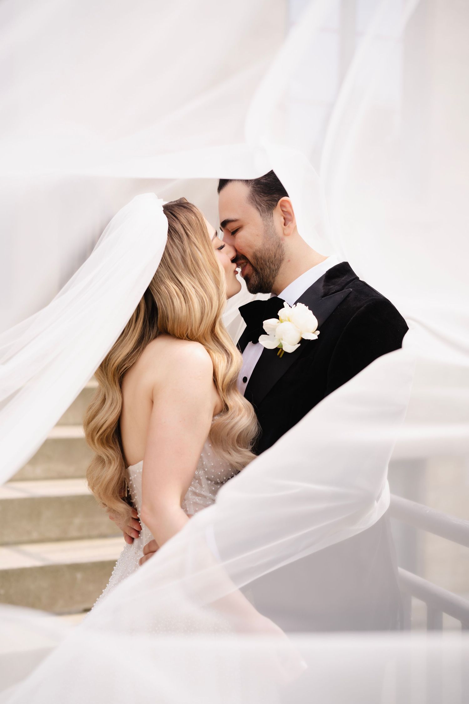Romantic wedding portrait of couple sharing intimate moment under flowing white veil.
