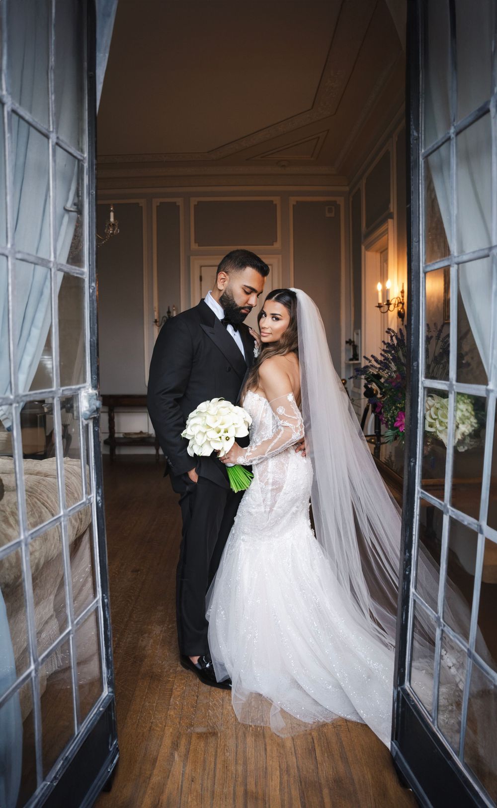 Wedding couple embracing in doorway of elegant venue with white bouquet.