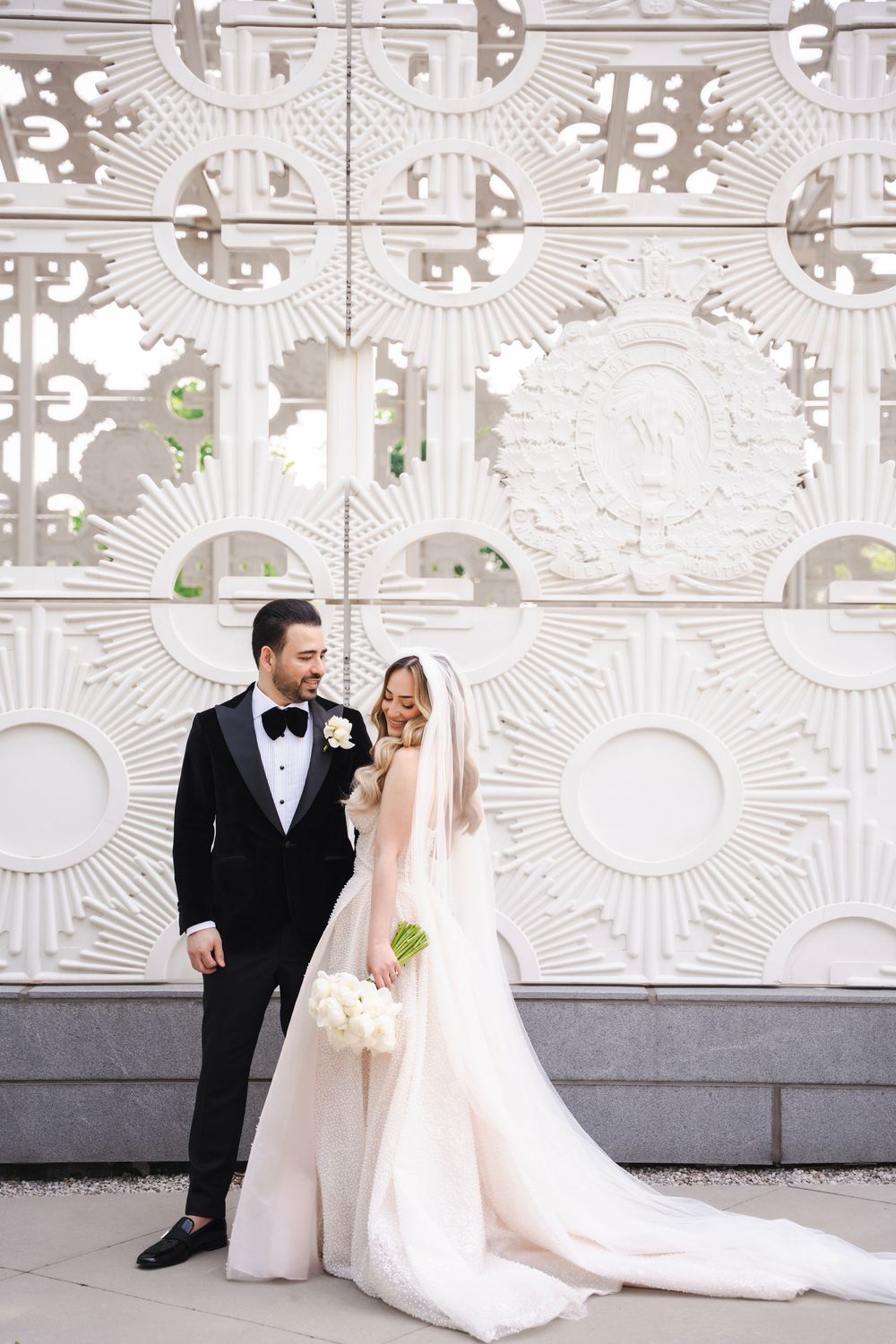 Wedding portrait of couple standing against decorative white architectural wall.