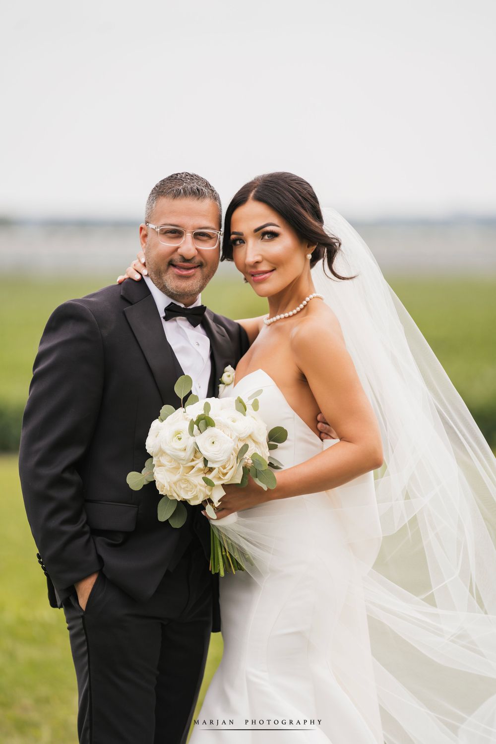 Wedding couple posing in formal attire against green field backdrop.