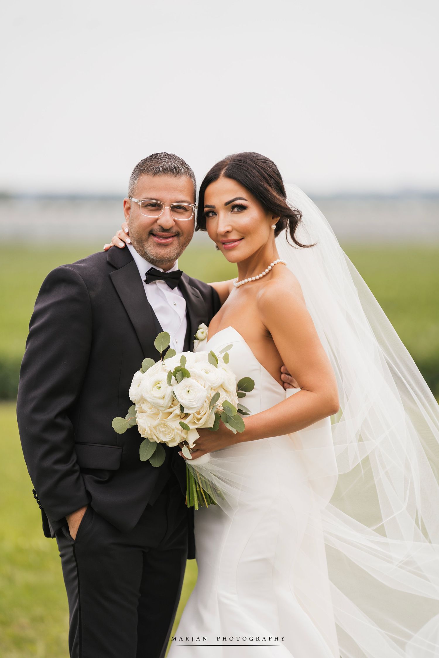 Wedding couple posing in formal attire against green field backdrop.