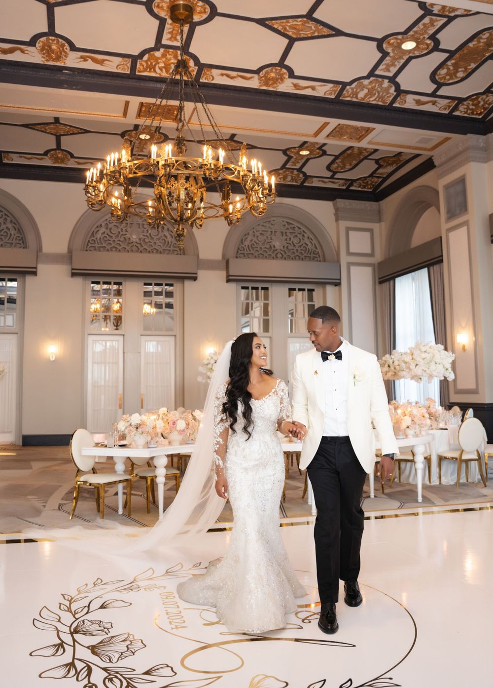 Elegant ballroom wedding reception setup with chandeliers and ornate floor design.