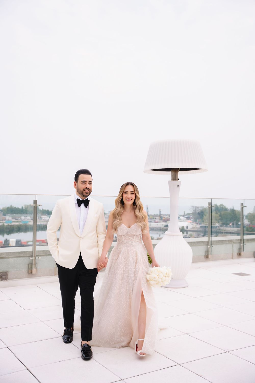 Couple walking on modern white rooftop terrace in formal wedding attire.