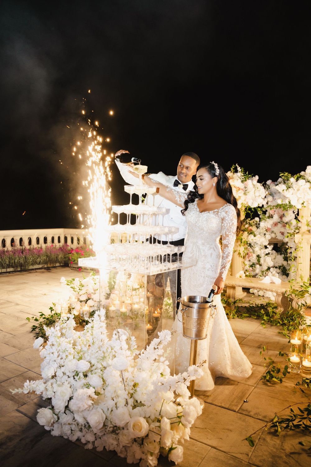 Couple celebrates with champagne tower and sparklers during nighttime wedding reception.