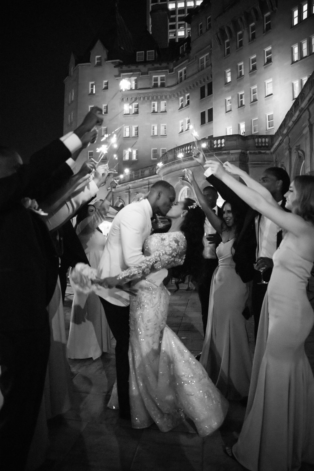 Black and white nighttime wedding reception with guests dancing and celebrating.