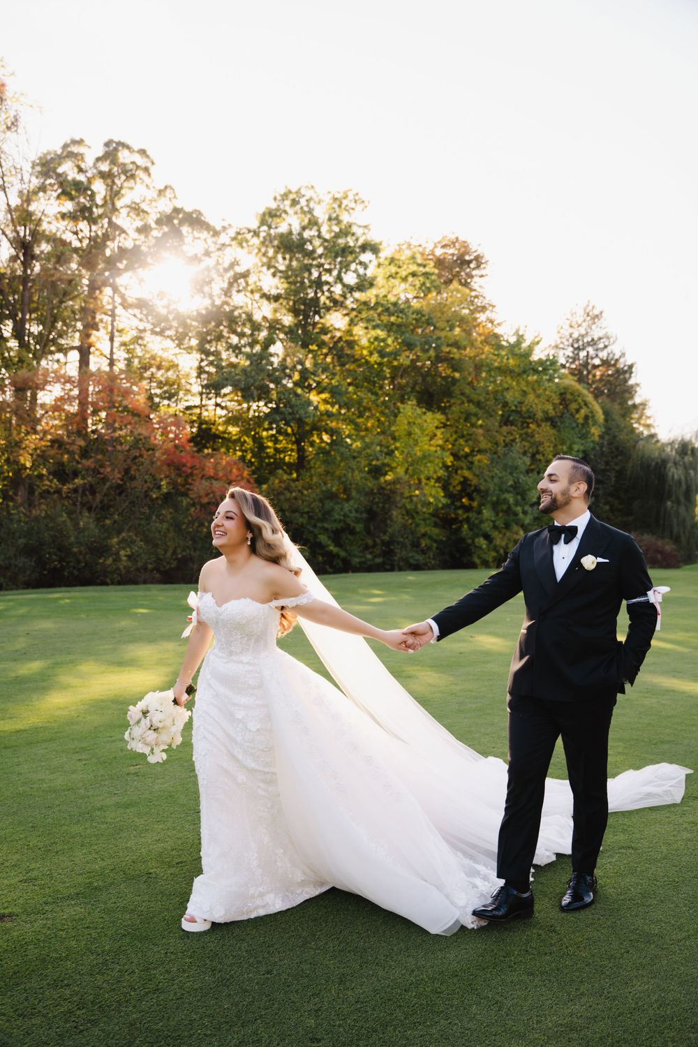Happy couple shares a playful moment on a manicured lawn during their wedding photoshoot.