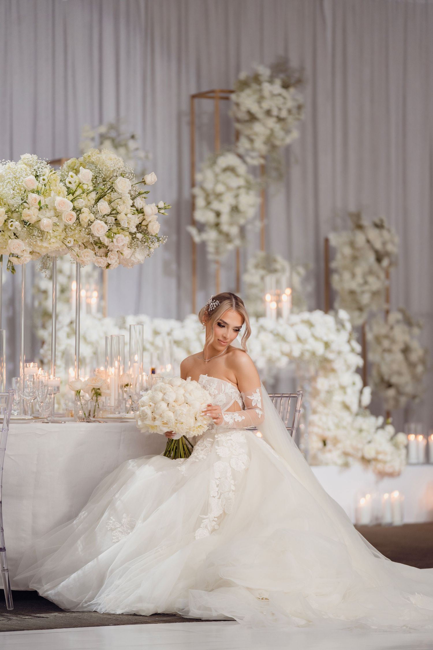 Luxurious wedding reception setup with white florals, crystal candelabras, and draped fabric backdrop.