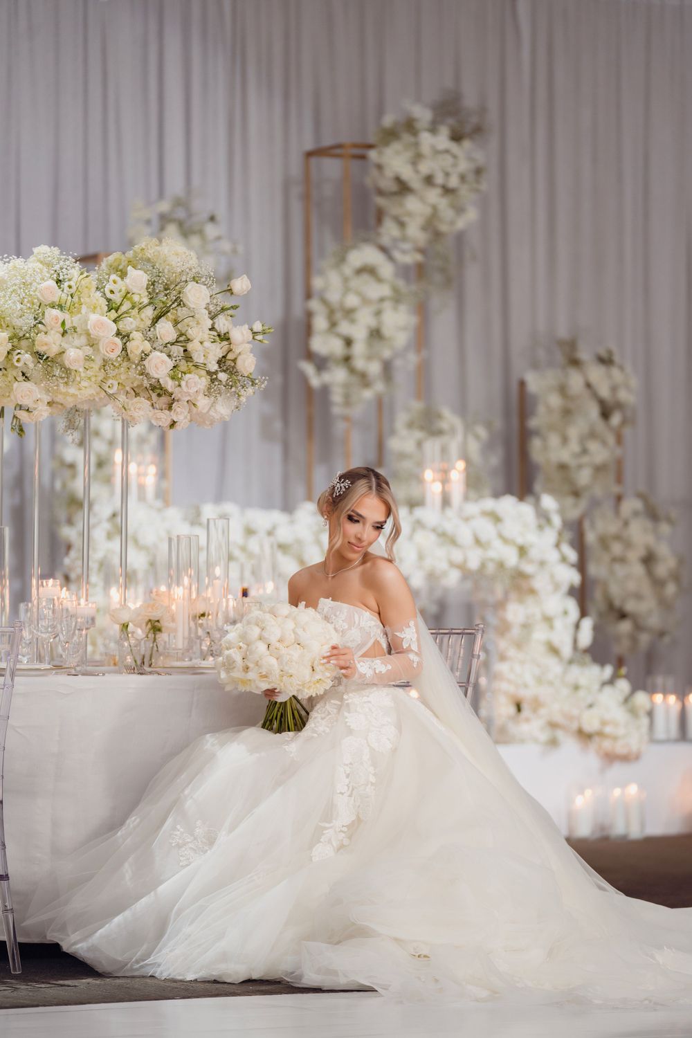 Luxurious wedding reception setup with white florals, crystal candelabras, and draped fabric backdrop.