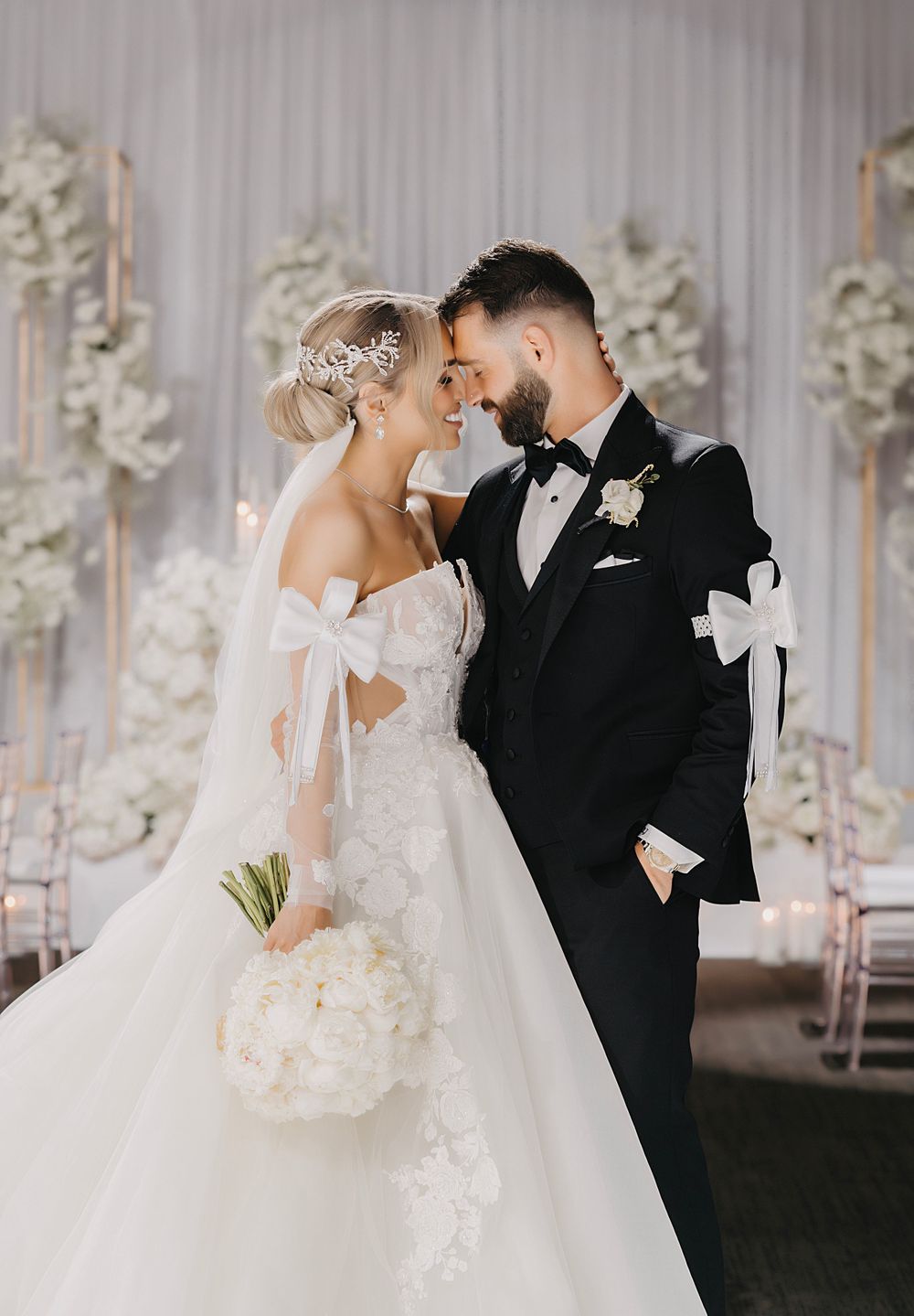 Intimate wedding moment captured in an elegant white room with floral arrangements.