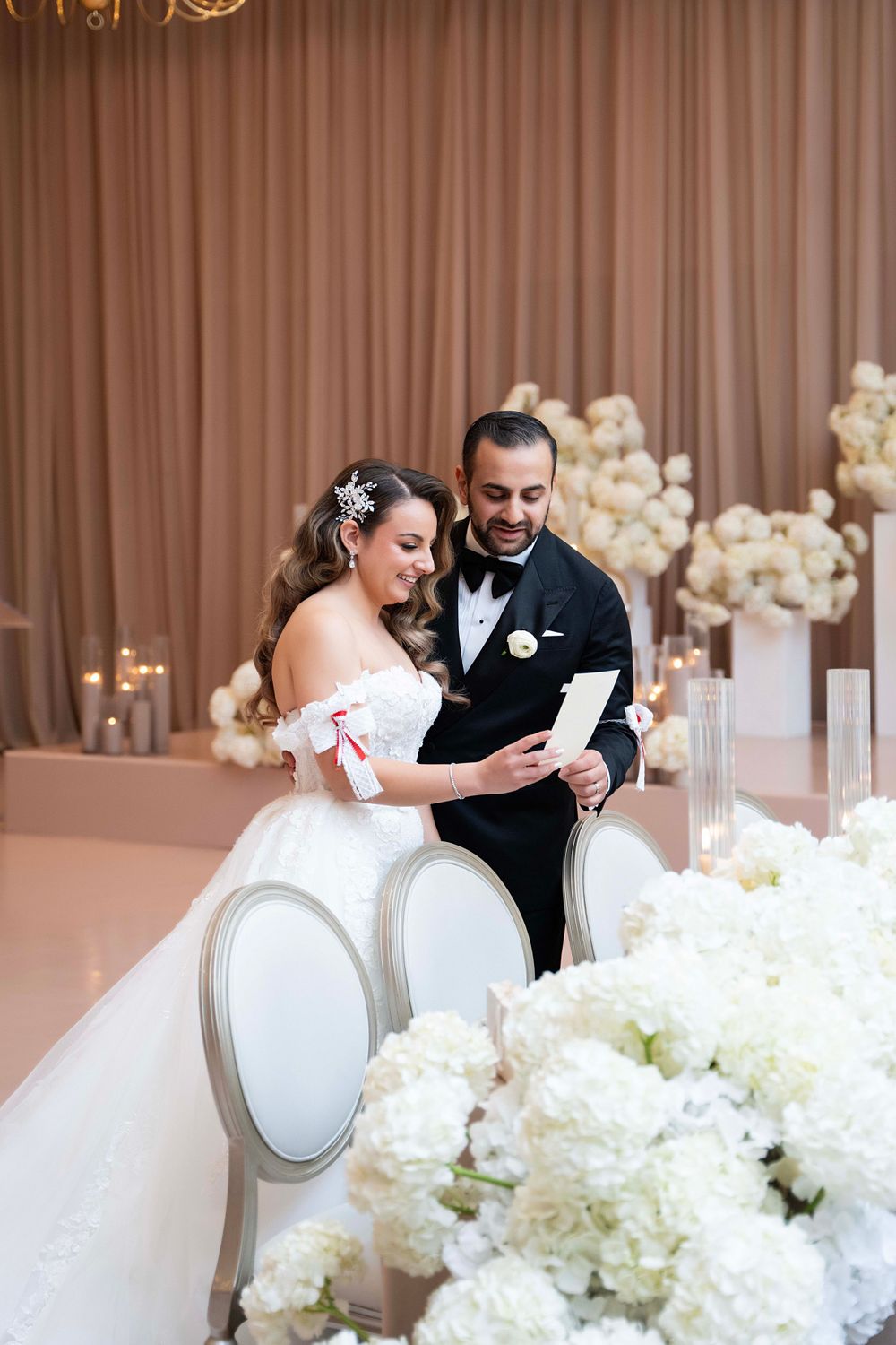 Wedding couple reads ceremony notes surrounded by elegant white floral arrangements and draping.