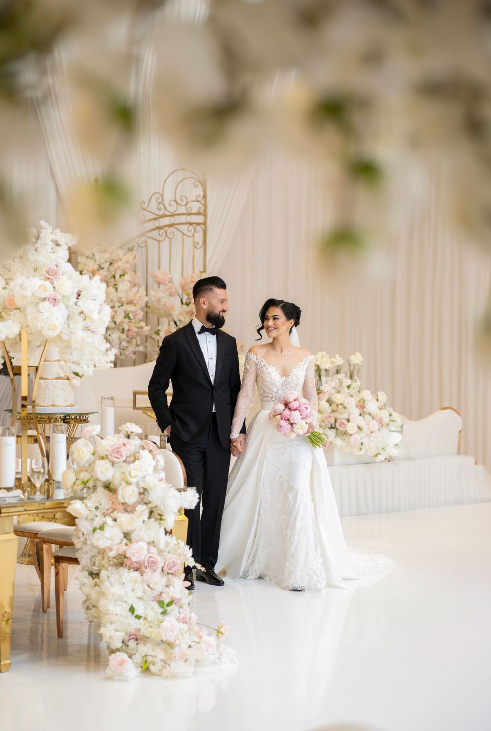 Romantic wedding scene in a luxurious white room adorned with pink and white floral arrangements.