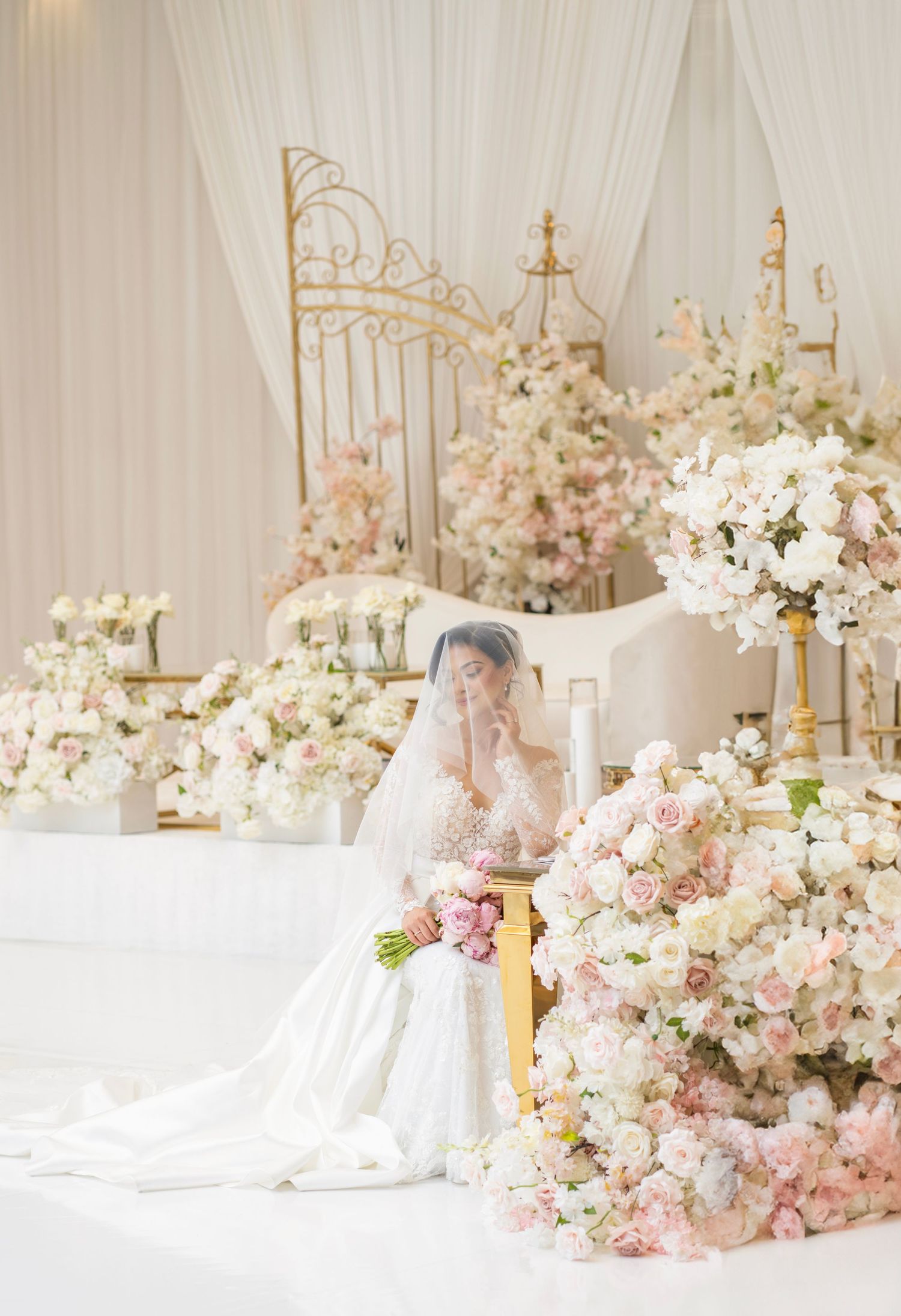 Dreamy wedding venue setup with white draping, golden decor elements, and cascading floral arrangements.