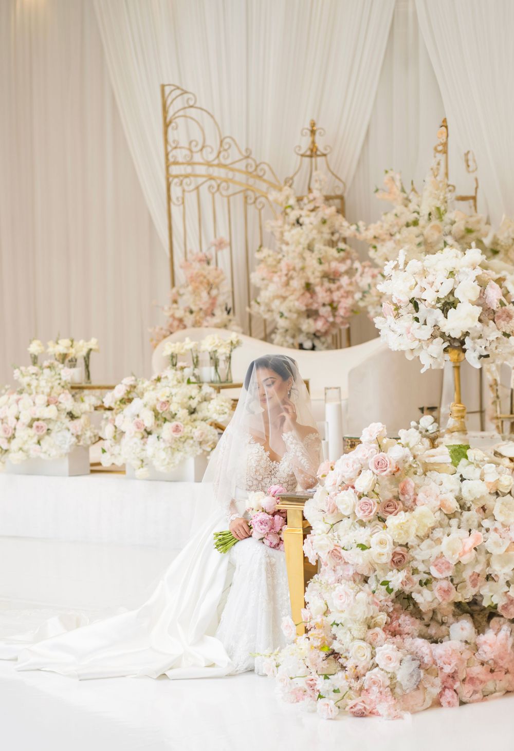 Dreamy wedding venue setup with white draping, golden decor elements, and cascading floral arrangements.